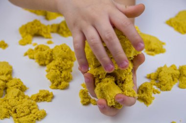 Çocukların elleri beyaz bir masada sarı kinetik kum oynuyor. Stres önleyici