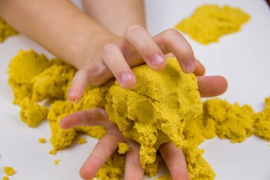 Çocukların elleri beyaz bir masada sarı kinetik kum oynuyor. Stres önleyici