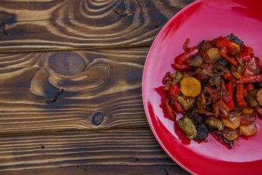 Kızarmış sebze sarımsaklı havuç soğan biberli kırmızı tabakta kahverengi ahşap arka planda et.