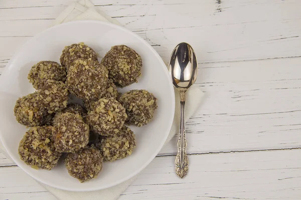 Energy balls homemade healthy candies without sugar in a white plate and a spoon on a cotton napkin on a white wooden background