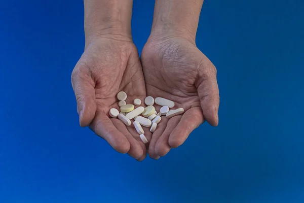 Handful of white pills and capsules of drugs in hands on a blue background