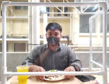 Maske takan erkekler, virüssel salgın hastalığın bulaşmasını önlemek için bir restoranın bölmesinde yemek yiyorlardı. Sosyal Mesafe ve Yeni Normal Konsept.