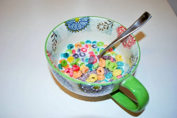 Close up of a bowl full of fruit flavored loops of sugar ready to eat breakfast cereal with a spoon sticking out