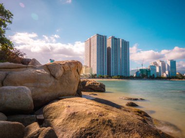 Sahilde kayalar, gökdelenler arka planda