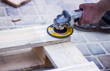 Marangoz atölyesindeki işçilerin portresini kapatıyoruz. Tahta yüzeyini zımpara değirmeniyle işliyoruz. Yakından çekilen fotoğrafçı marangoz ahşap bir tahtayı cilalıyor, çalışma yerinde öğütüyor..