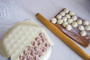 Geleneksel Rus pişmemiş pelmeni tahtada ve ev yapımı pelmeni malzemeleri beyaz masada. Pelmeni, ravioli veya etli hamur tatlısı yapma süreci. Uzayı kopyala Yan görünüm.