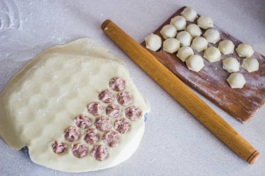 Geleneksel Rus pişmemiş pelmeni tahtada ve ev yapımı pelmeni malzemeleri beyaz masada. Pelmeni, ravioli veya etli hamur tatlısı yapma süreci. Uzayı kopyala Yan görünüm.