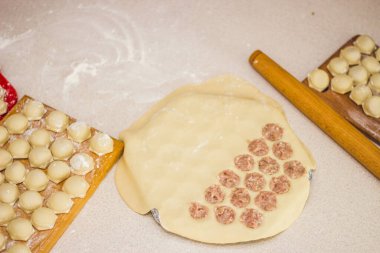 Geleneksel Rus pişmemiş pelmeni tahtada ve ev yapımı pelmeni malzemeleri beyaz masada. Pelmeni, ravioli veya etli hamur tatlısı yapma süreci. Uzayı kopyala Yan görünüm.