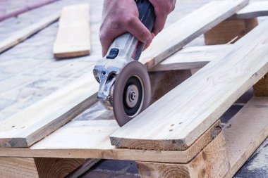 Eski ahşap tahtaları öğütücüyle onar. Bir marangoz ve marangozluk atölyesinde çalışan küçük bir büstiyer kapatıyoruz. Marangoz ahşapla çalışır. Yan görünüm.