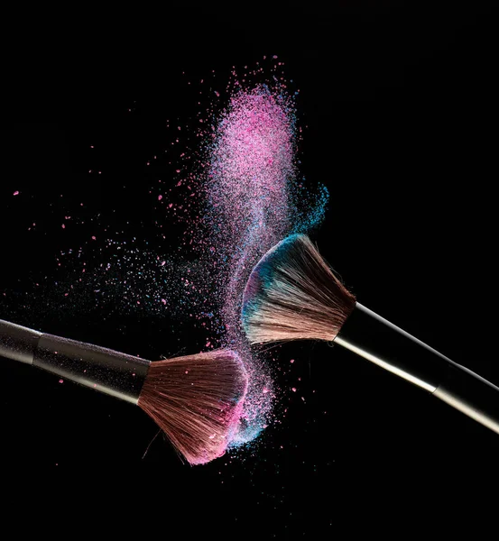 Brosses de maquillage avec explosion de poudre rose et bleue sur bac noir — Photo