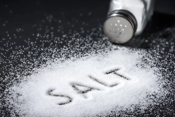 Ordet salt skrivs in en hög med vit salt och salt shaker — Stockfoto