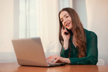 Genç, sevimli iş kadını ofiste oturuyor ve dizüstü bilgisayar kullanıyor. Dizüstü bilgisayarla çalışan genç bir kadın. Evde internete bağlanan serbest çalışan kadın..