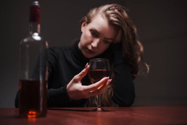 Depresyonda olan genç ve güzel bir kadın, alkol içiyor. Taciz ve alkolizm kavramı. Alkolik kadın bir şişe şarap ve bir bardak şaraptan içiyor. Cam üzerine seçici odaklanma.