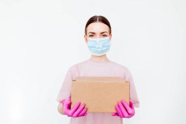 Coronavirüs salgını sırasında teslimat. Uzayı kopyala Teslimatçı kadın elinde plastik eldivenli karton kutular ve beyaz arka planda maske tutuyor. Çevrimiçi alışveriş ve ekspres tıbbi teslimat .