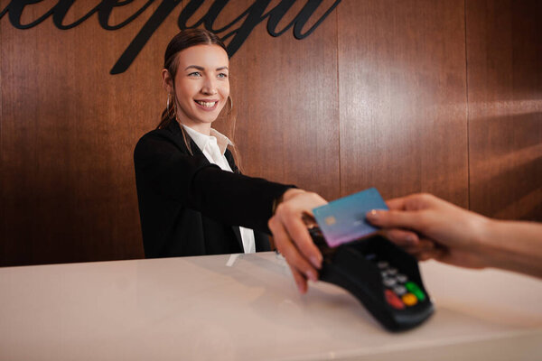 Рука клиента, платящего бесконтактной кредитной картой по технологии NFC. Счастливая женщина держит банковский терминал в роскошном магазине, отеле или ресторане
.