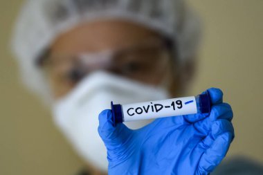 Koruyucu giysili bir kadın test tüpü tutuyor. Coronavirus COVID 19 2019-nCoV.