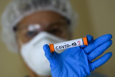 Koruyucu giysili bir kadın, Coronavirus COVID 19 virüsü taşıdığından şüphelenilen bir test tüpü tutuyor. Kavram.