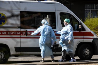 Koronavirüs COVID-19 'a karşı koruyucu giysiler giyen ambulans doktorları Ukrayna, Kyiv' de ambulans arabasının yanında. 