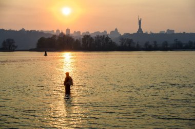 Balıkçı Dinyeper nehrinde duruyor. Gün batımı Kyiv ve Anavatan Anıtı üzerinde. 