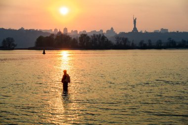 Balıkçı Dinyeper nehrinde duruyor. Gün batımı Kyiv ve Anavatan Anıtı üzerinde. 