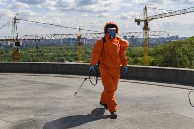 Koruyucu giysili adam COVID 19 'un yayılmasını önlemek için dezenfektan sıkar. Kyiv, Ukrayna Mayıs 2020