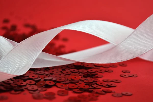 White satin ribbon with sparkles on red background. Festive concept.