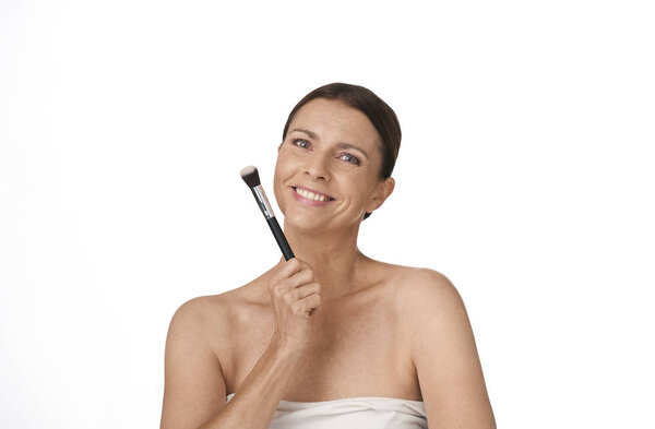Woman looking happy confident smiling holding a make up brush in her hand on white background