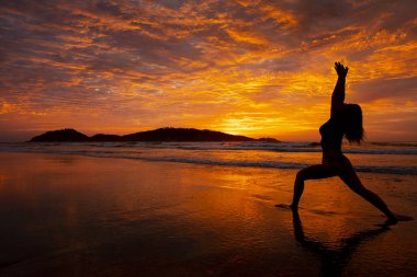 Yoga yapan kadın gün doğumunda Florianopolis Brezilya 'daki Campeche plajında poz veriyor.