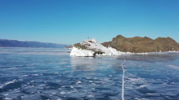 Lago Baikal congelado, cabo Horin-Irgi de la isla Olkhon. Hermoso paisaje de invierno con hielo suave y claro cerca de la costa rocosa. El famoso hito natural de Rusia. Hielo azul transparente con grietas profundas . — Vídeo de stock