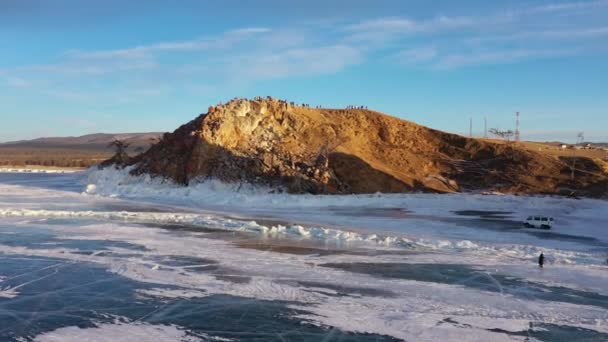Lac Baïkal gelé, cap Burhan Rocher chaman de l'île Olkhon. Touristes sur le lac Baïkal, marchant sur la glace du lac.. Le célèbre monument naturel de la Russie. Glace transparente bleue avec fissures profondes . — Video