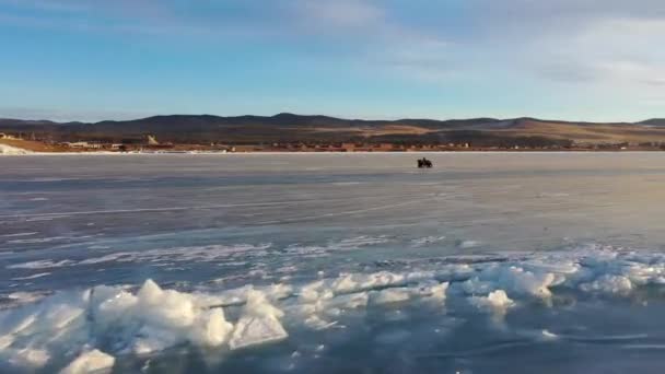 Zamarznięte jezioro Bajkał, transport na kołach na lodzie jeziora. Turyści nad jeziorem Baikal, spacerujący po lodzie jeziora.. Słynna krajobrazowa Rosja. Niebieski przezroczysty lód z głębokimi pęknięciami. — Wideo stockowe