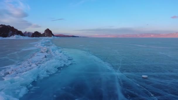 Lago congelado Baikal, lago Baikal hummocks. Hermoso paisaje de invierno con hielo suave y claro cerca de la costa rocosa. El famoso hito natural de Rusia. Hielo azul transparente con grietas profundas . — Vídeos de Stock