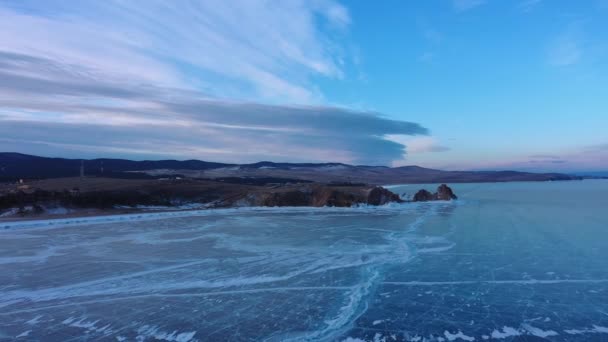 Замерзшее озеро Байкал, мыс Бурхан-Шаман на острове Ольхон. Зимний пейзаж с прозрачным гладким льдом у скального берега. Знаменитая природная достопримечательность России. Голубой прозрачный лед с глубоким краком — стоковое видео