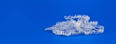 Mavi arka planda görünmez ortodonti kozmetik parantez, diş hizalayıcılar, plastik diş telleri. Güzel bir gülümsemeye ve beyaz dişlere sahip olmanın bir yolu..