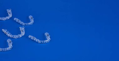 Mavi arka planda görünmez ortodonti kozmetik parantez, diş hizalayıcılar, plastik diş telleri. Güzel bir gülümsemeye ve beyaz dişlere sahip olmanın bir yolu..