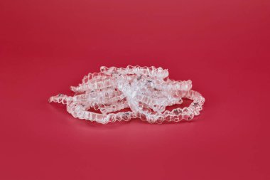Kırmızı arka planda görünmez ortodonti kozmetik parantez, diş hizalayıcılar, plastik diş telleri. Güzel bir gülümsemeye ve beyaz dişlere sahip olmanın bir yolu..
