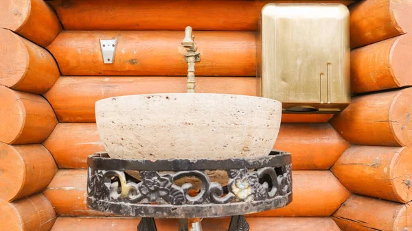 Um lavatório de pedra em um suporte de metal forjado em uma casa de madeira. Interior em uma casa feita de madeira . — Fotografia de Stock
