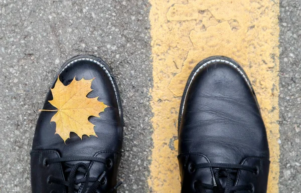 Een mooie combinatie van een geel esdoorn herfstblad naast de gele wegmarkeringen en de poten van een meisje in zwarte laarzen in het park. Herfst concept, mooie achtergrond met kopieerruimte — Stockfoto