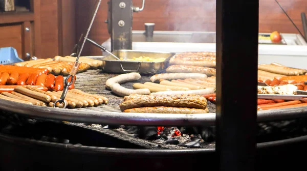 Salsichas fritas. Um restaurante de rua. Muitas salsichas grelhadas em um grande churrasco redondo em um festival de comida de rua. Churrasqueira na banca de comida Mercado de Natal . — Fotografia de Stock