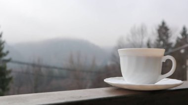 Soyut doğa arka planında beyaz bir fincan kahve. Bir kahve fincanı balkonda, arkası doğa manzaralı. Otel balkonunda içkili seramik bardak.