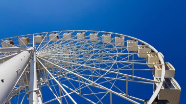 Mavi gökyüzüne karşı büyük beyaz dönme dolap. Fotokopi alanı olan mavi arkaplandaki cazibenin bir parçası. Kulübeler, izleme platformları.