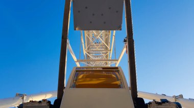 Mavi gökyüzüne karşı büyük beyaz dönme dolap. Fotokopi alanı olan mavi arkaplandaki cazibenin bir parçası. Kulübeler, izleme platformları.