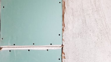 Alçıpandan yapılma inşaat halindeki bir binanın tamamlanmamış duvarı. Duvarın bir kısmı alçıpanla kaplanmış. Alçıpan alçı beklentisiyle duvara sabitlenir.