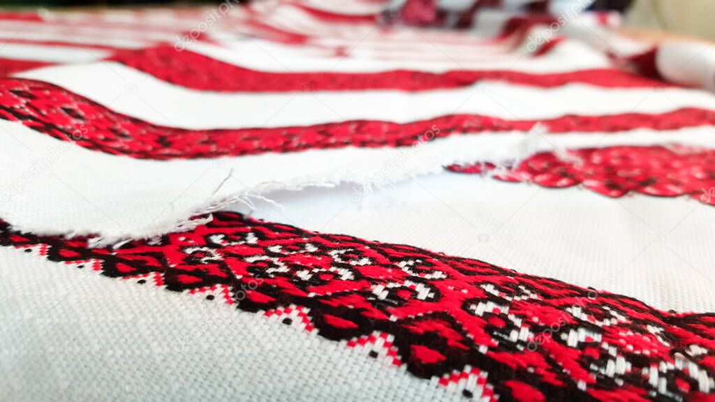 Ukrainian folk hand embroidery. Embroidered ornament with red-black threads on white fabric. Embroidered ornament in black and red thread. Ethnic Ukrainian folk embroidery on white fabric.