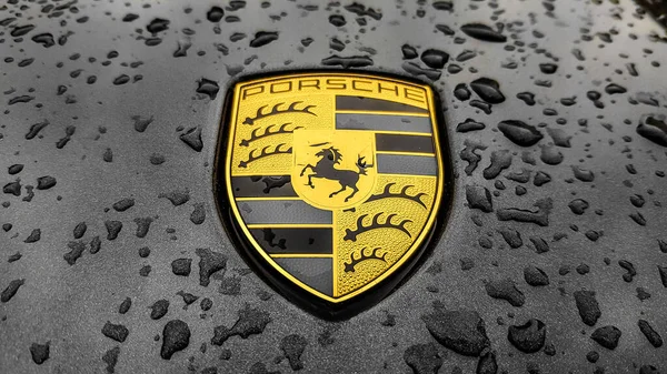 ウクライナ キエフ 2020年3月27日 ポルシェのロゴは 雨滴と黒の車に閉じます スポーツカーのフードエンブレム コピースペース編集写真 路上でドイツ車の展示会 — ストック写真
