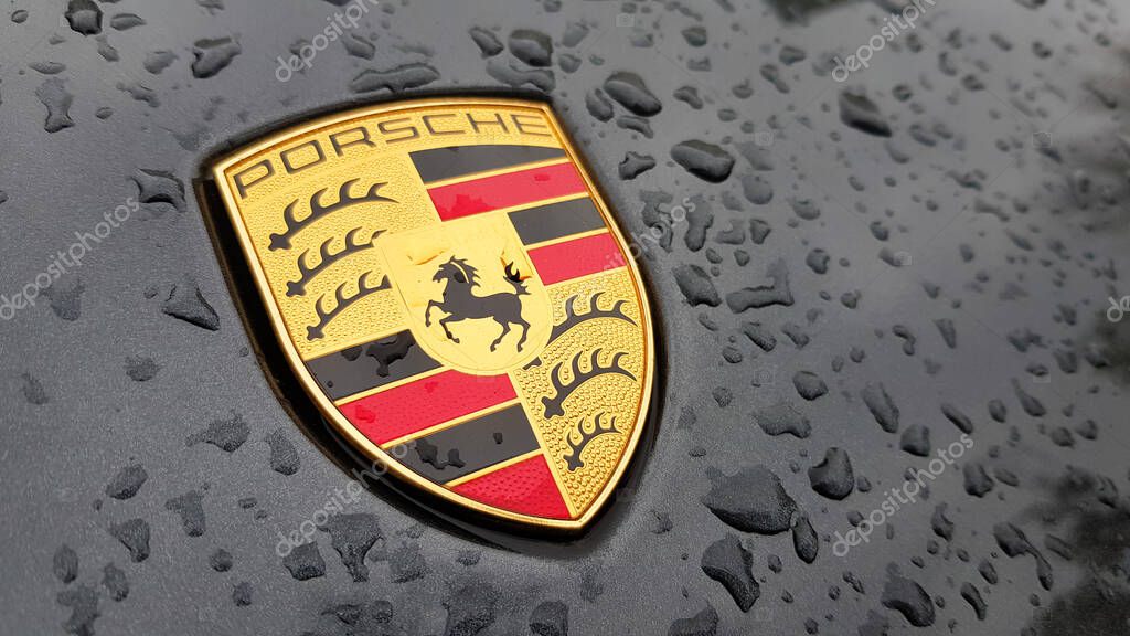 Ukraine, Kiev - March 27, 2020: Porsche logo close up on a black car with raindrops. Hood emblem of a sports car. copy space, editorial photography. German car exhibition on the street