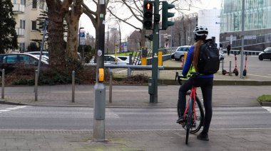 Almanya, Düsseldorf - 28 Şubat 2020: Kasklı genç bir kız, trafik ışıklarında durdu ve caddeyi geçmek için bir izin sinyali bekledi. Şehir görünümü