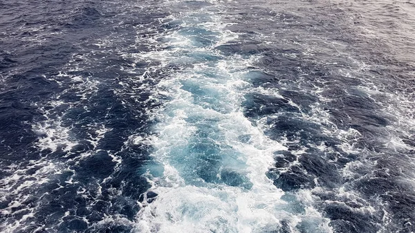 Cruise ship or trail on the surface of the blue red sea. Sea water ship trail with white foamy wave. Top view of the deep ocean. Perspective of a wave of white water