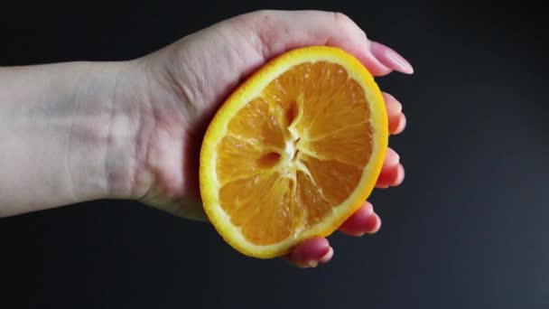 新鮮なジューシーなオレンジの半分を女性の手で絞る 黒の背景にオレンジパルプから滴下柑橘類のオレンジジュース 健康的な食事 さわやかな飲み物の準備の概念 — ストック動画