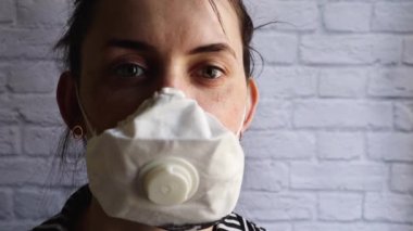 Coronavirüs salgınından kalma maske takmış genç bir kadının portresi beyaz tuğla bir duvara karşı. Covid-19 sağlık ve güvenlik konsepti, H1H1 virüsüne karşı koruma. Uzayı kopyala Heyecanlı bak.